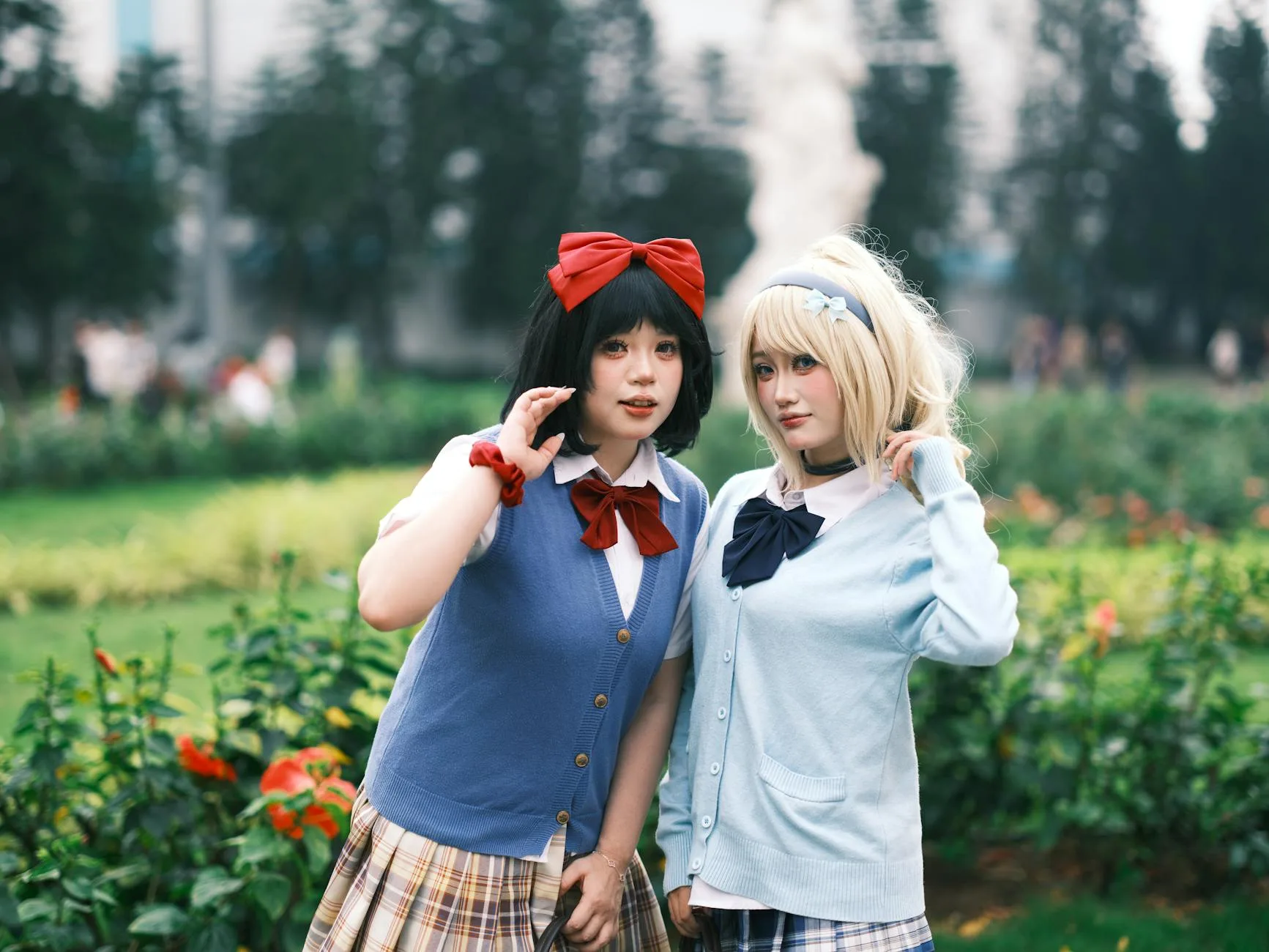 Dwie młode cosplayerki w szkolnych mundurkach pozują w ogrodzie